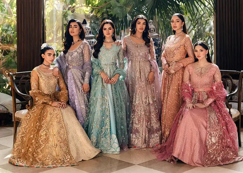 Six models wearing elegant Pakistani bridal and formal suits in pastel colors including gold, lavender, mint green, beige, peach, and pink, featuring intricate embroidery and embellishments, seated and standing in a luxurious indoor setting