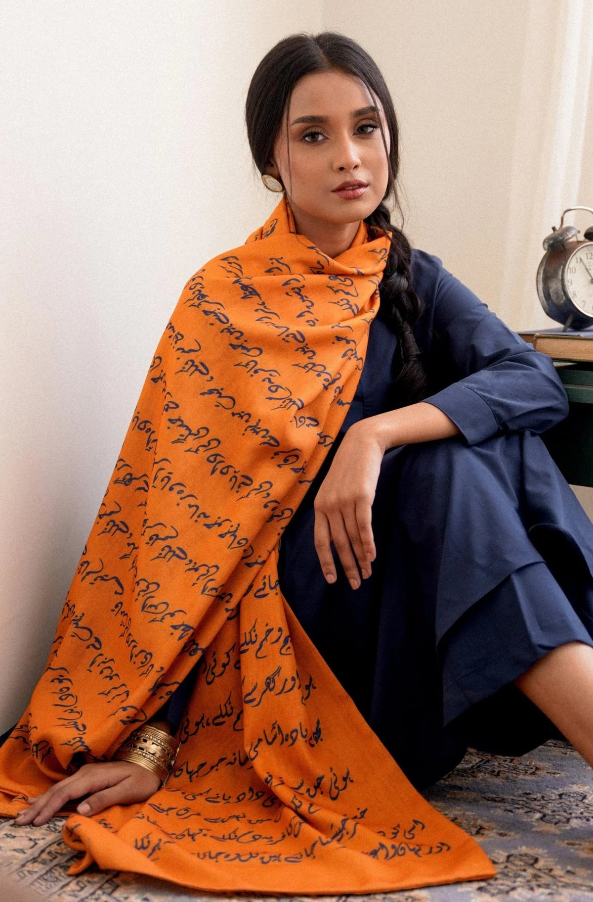 Close-up styling shot of orange Armaan stole with Urdu poetry print, draped elegantly over navy outfit, highlighting the literary-inspired design