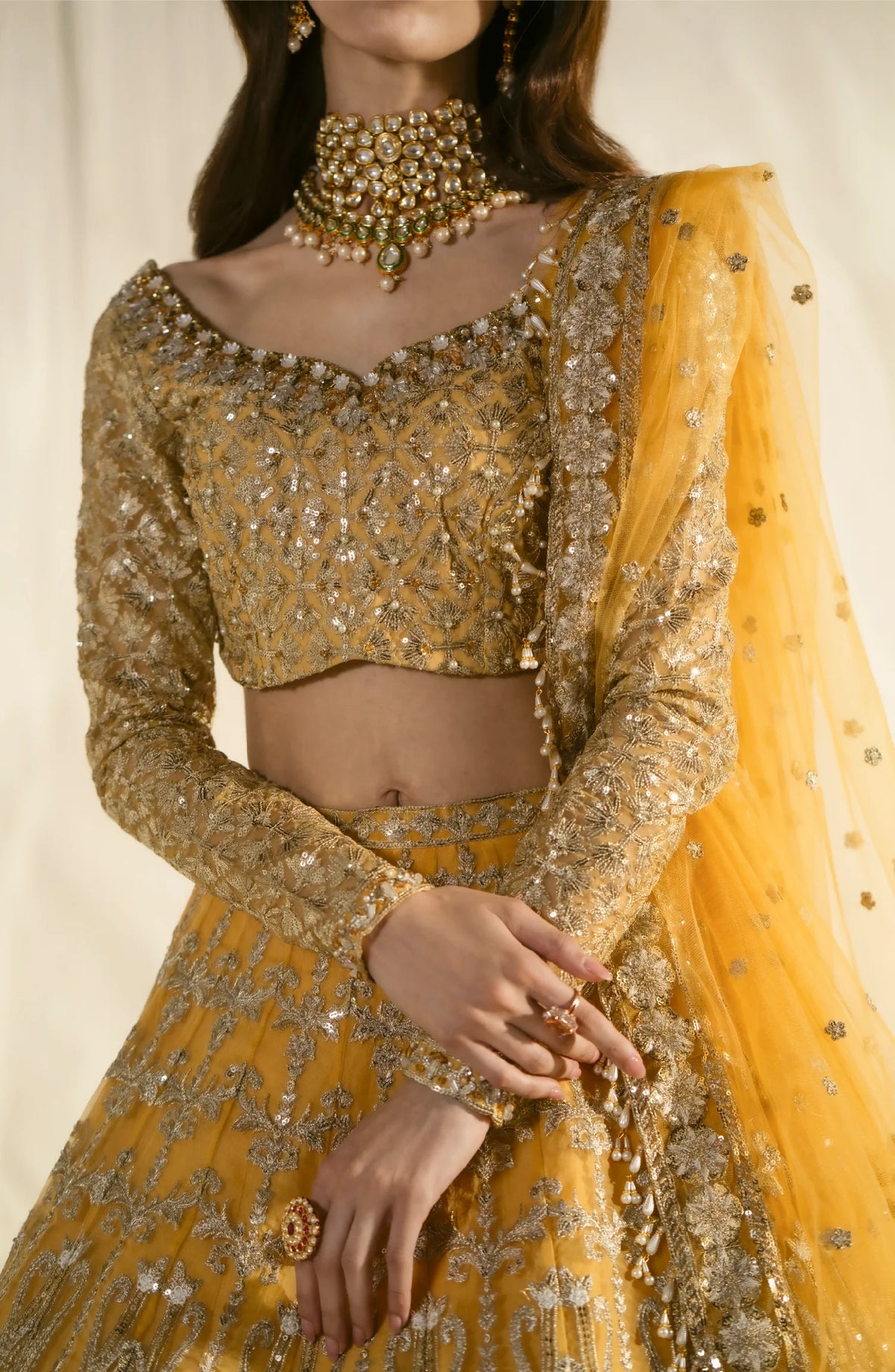 Close-up detail of golden lehenga blouse featuring elaborate embroidery, beadwork, and traditional jewelry including statement choker necklace.