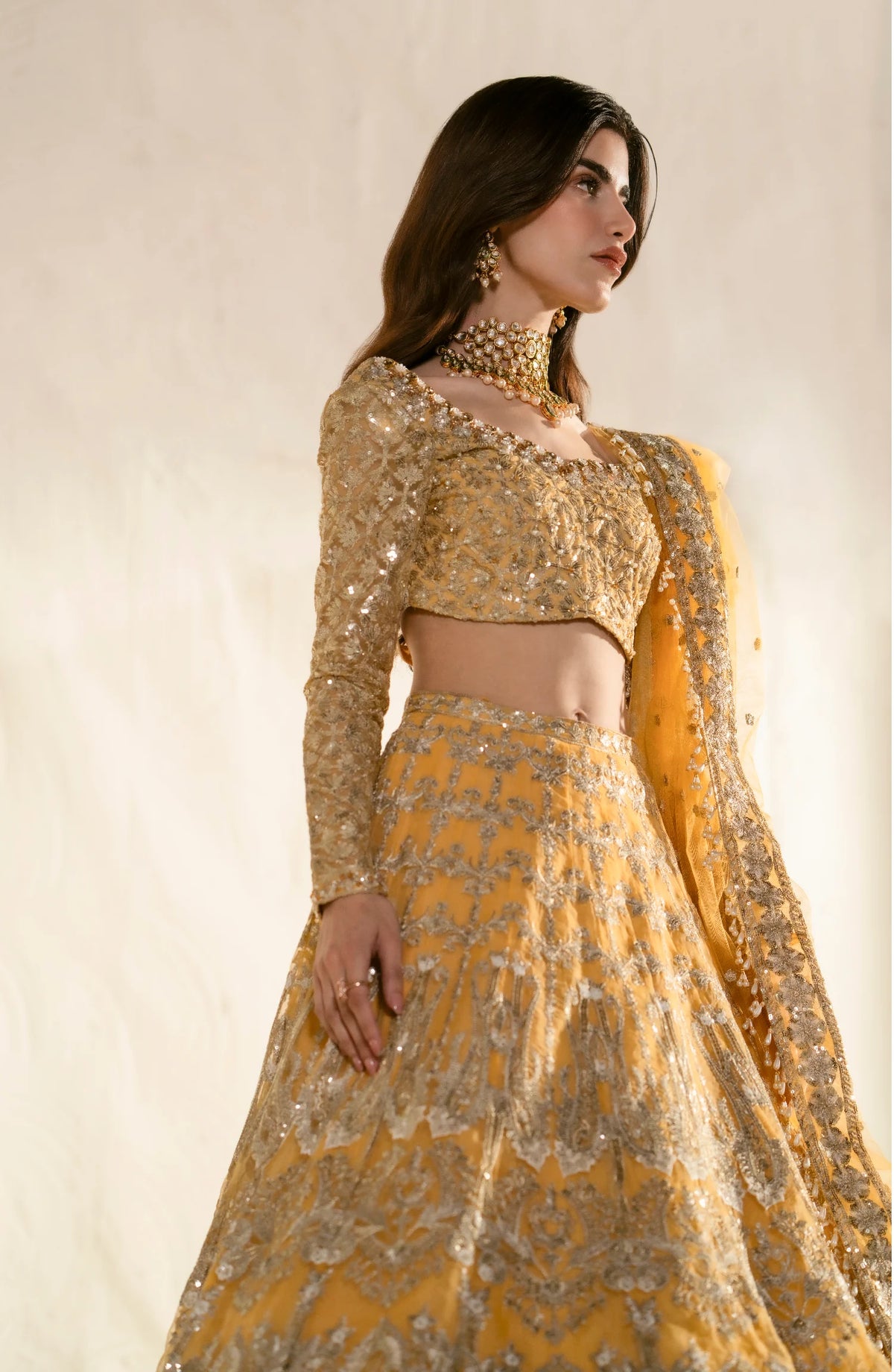 Three-quarter view of golden embroidered lehenga set showcasing intricate beadwork, sequin details, and traditional Pakistani bridal wear with ornate jewelry.