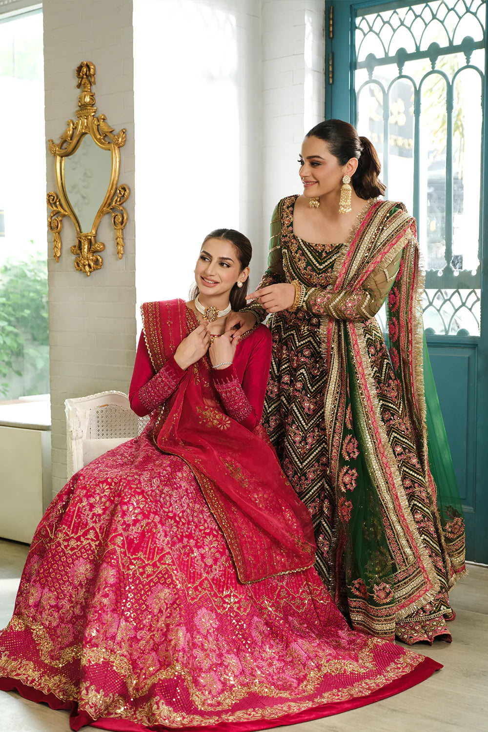 Saira Rizwan bridal collection lifestyle shot - two models in fuchsia pink and green designer lehengas - Pakistani wedding wear Canada.