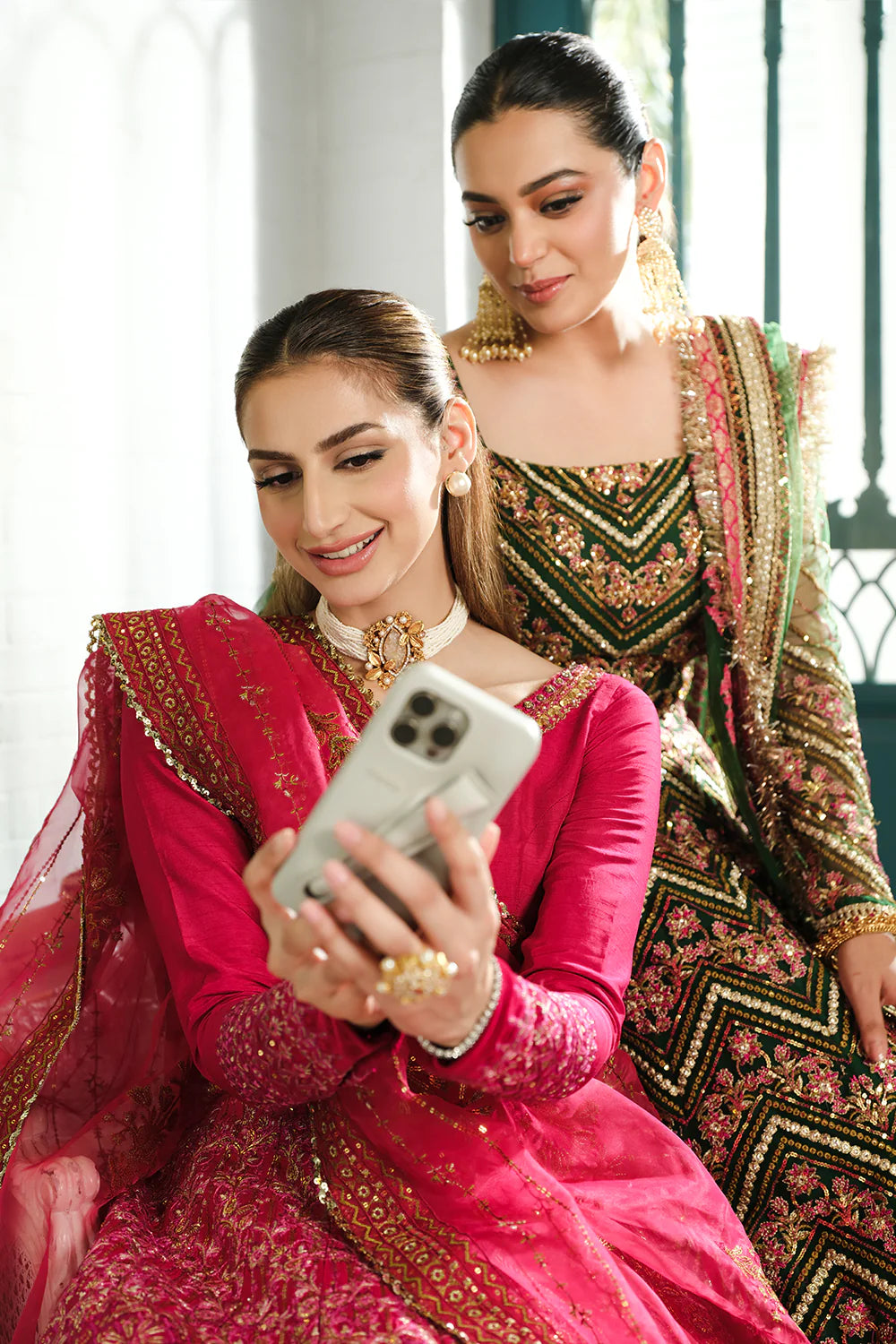 Saira Rizwan bridal collection selfie moment - models in fuchsia pink and green designer lehengas taking photo - Pakistani wedding wear lifestyle Canada.