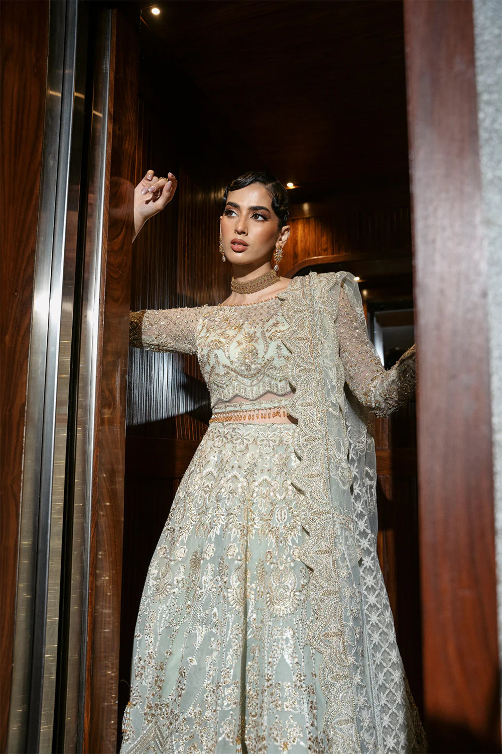 Dramatic pose of Pakistani bridal dress with Chinese Silver embroidery against modern glass doors, highlighting the contrast between traditional craftsmanship and contemporary architecture
