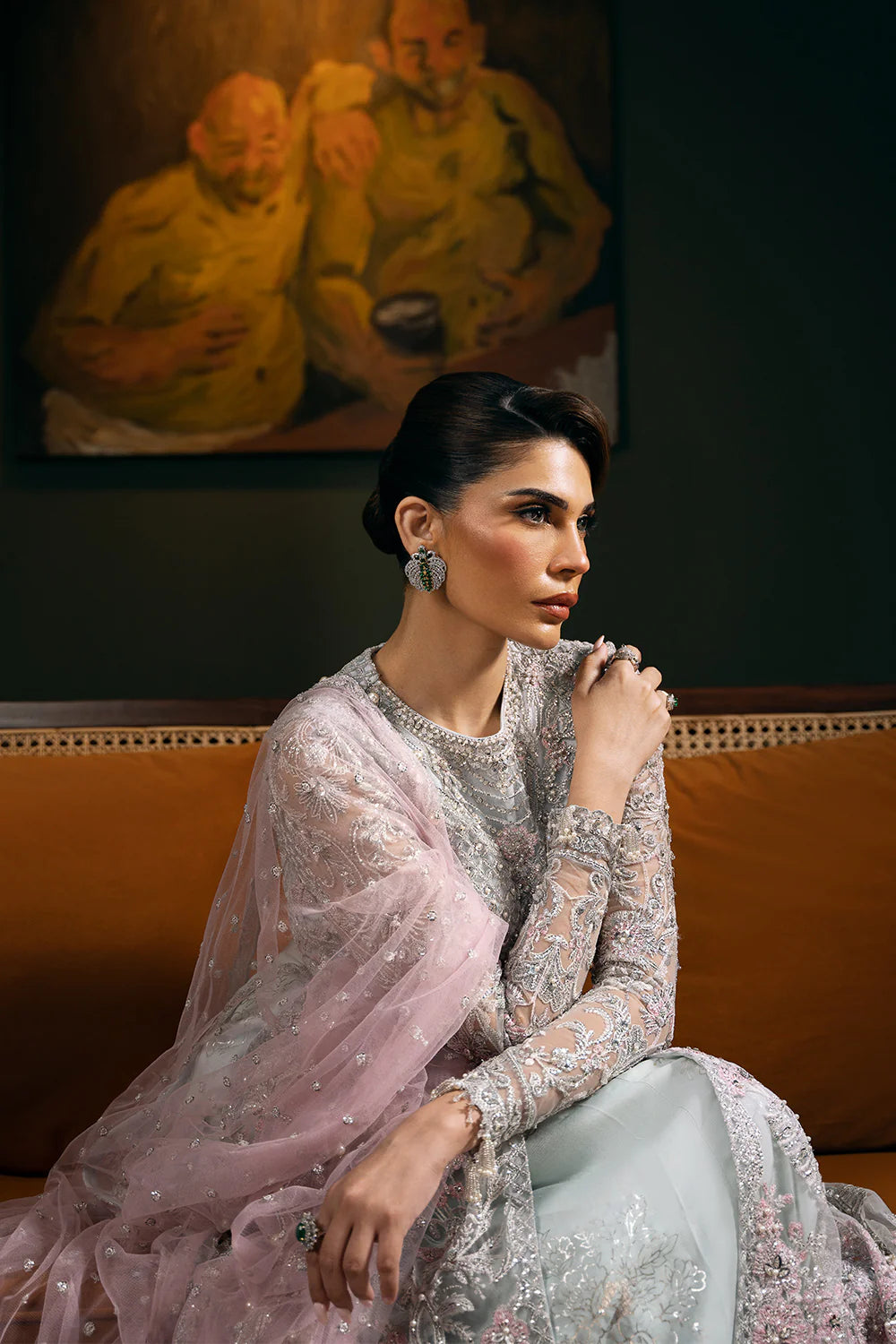 Elegant seated portrait in Saira Rizwan bridal dress featuring detailed embroidered sleeves, sheer dupatta, and traditional Pakistani bridal jewelry