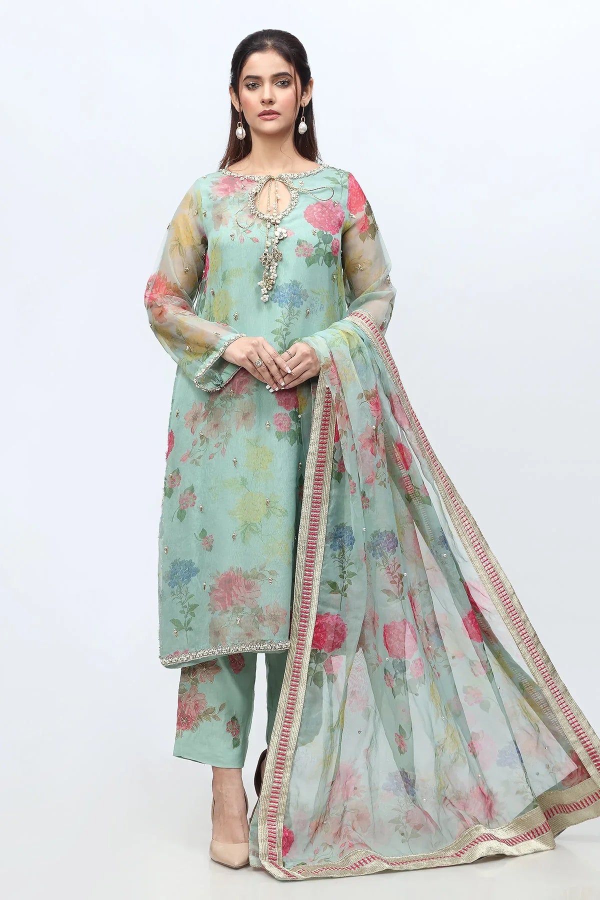 Woman in an olive green Pakistani and punjabi suit with gold embroidery Traditional South Asian interior with floral and carved wooden elements. Brand 'ASIM JOFRA' visible