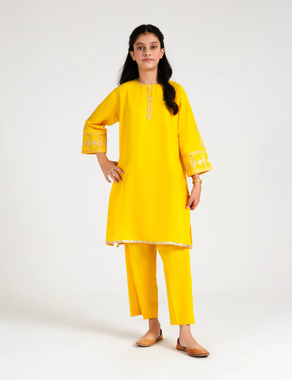 A 9-10-year-old girl wearing a yellow embroidered lawn suit from Beechtree – a stylish pick for Pakistani suits online in Canada.