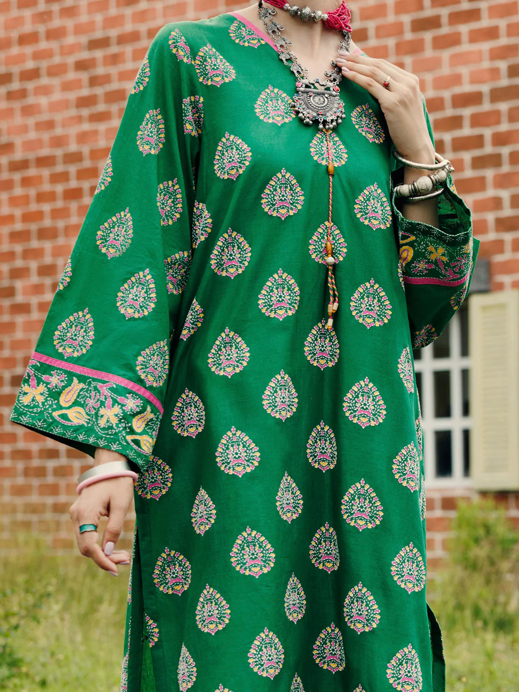 Woman standing front view full length hands at sides emerald green paisley lawn kurti floral hem border Almirah Eid festive Pakistani suits Canada