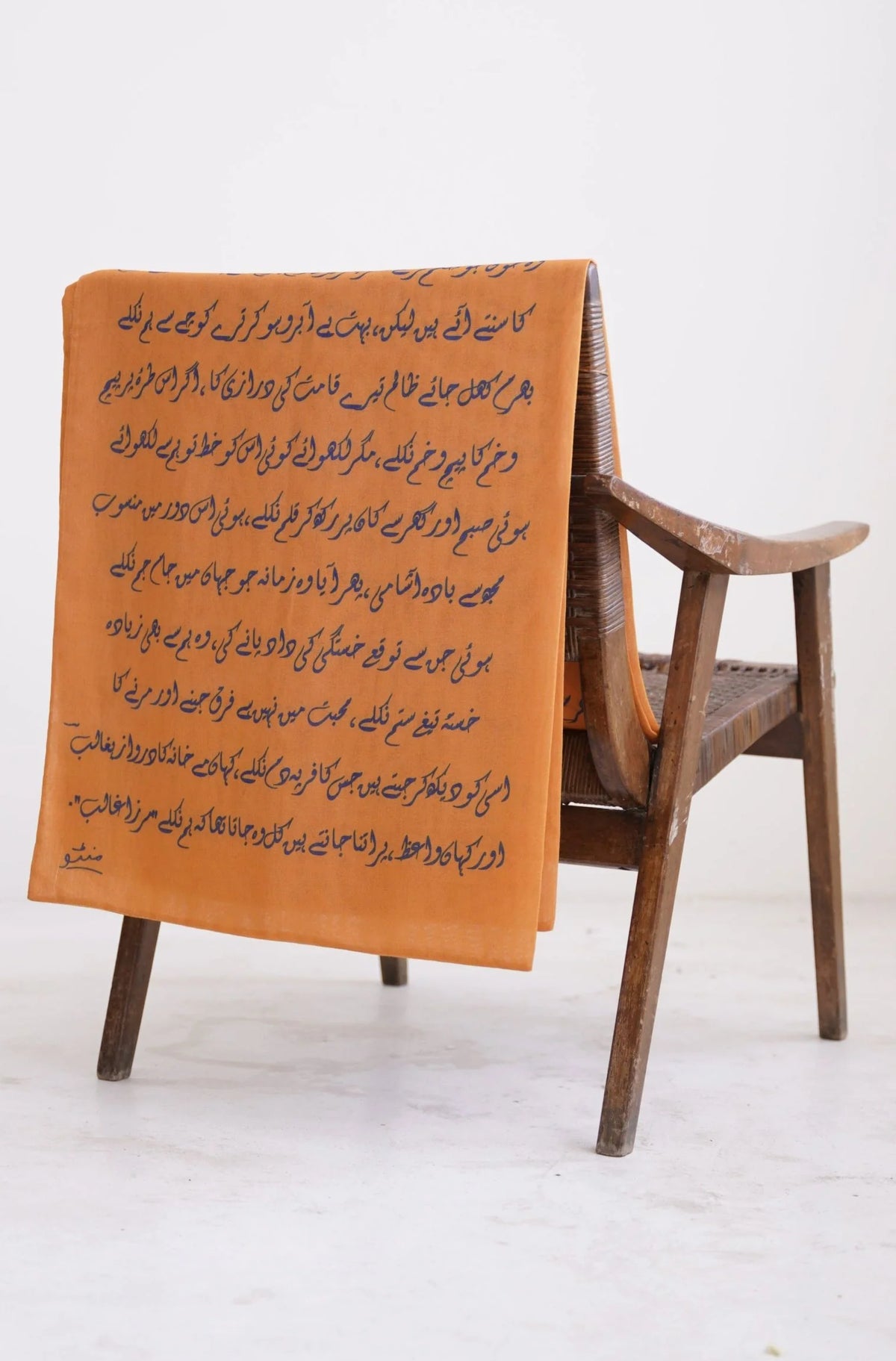 Orange Armaan stole displaying complete Urdu poetry text from Mirza Ghalib, draped on wooden stool showing full literary calligraphy design from Manto Karvaan collection
