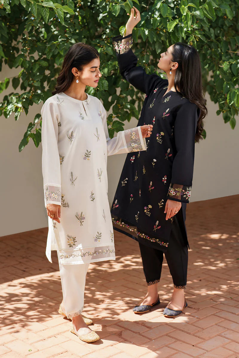 Close-up intimate shot of two models wearing Baroque floral embroidered lawn suits in off white and black, displaying detailed sleeve embroidery and traditional styling