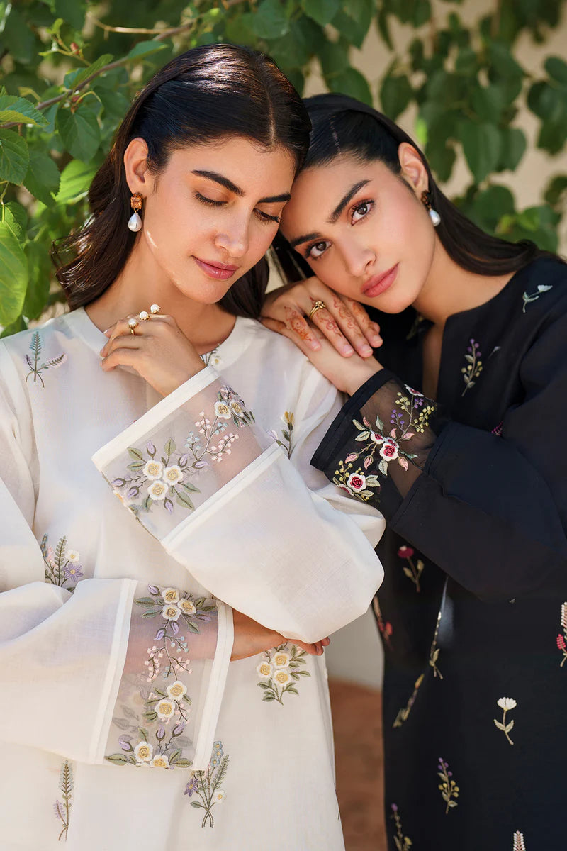 Two models in elegant pose wearing Baroque embroidered lawn suits - off white and black floral sets showcasing intricate Pakistani formal wear craftsmanship