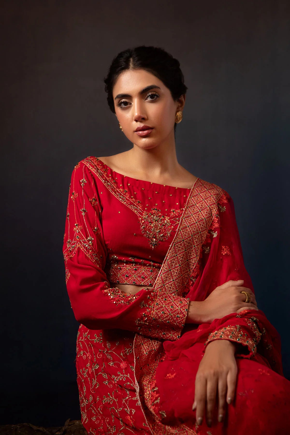 women sitting showing the Close-up of Kayseria’s maroon 3PC suit, highlighting the detailed embellishments on the kurti and lehenga.