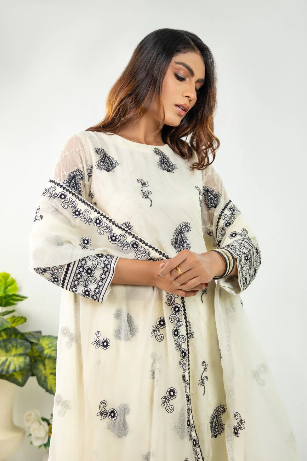 A woman wearing a white chiffon embroidered shirt with floral and geometric patterns, paired with a dupatta and crepe pants.