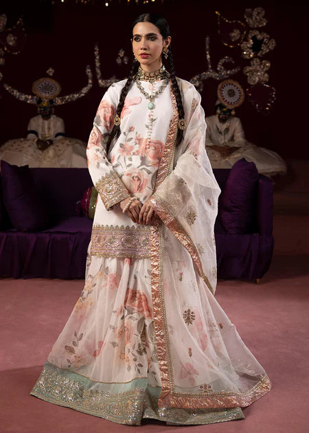 Elegant white floral printed sharara set with pink roses, gold embroidery borders, and traditional Pakistani formal wear styling.