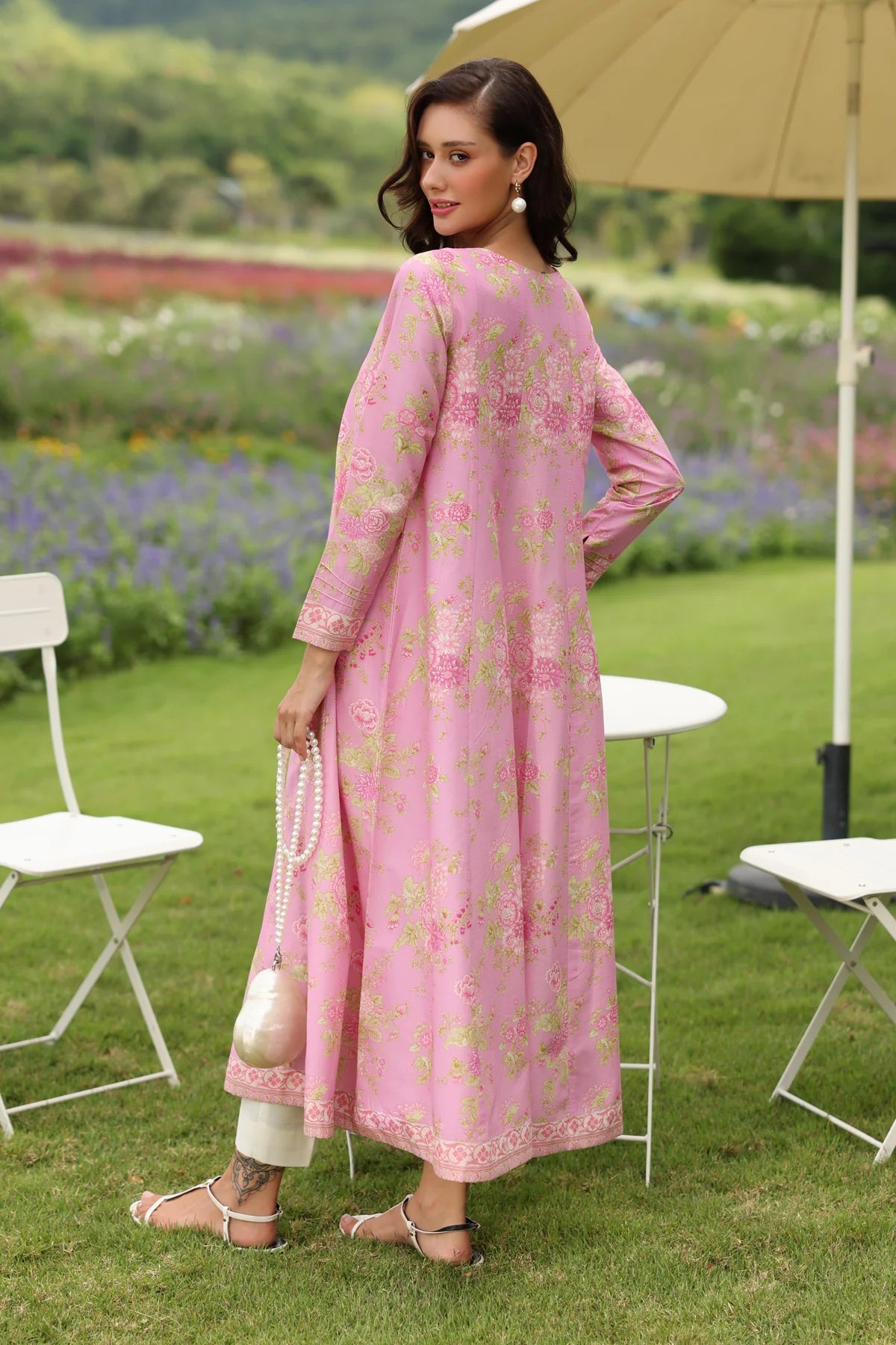 Woman standing full length back view Xenia pink printed lawn gown embroidered hem border white trouser Pakistani suits Canada