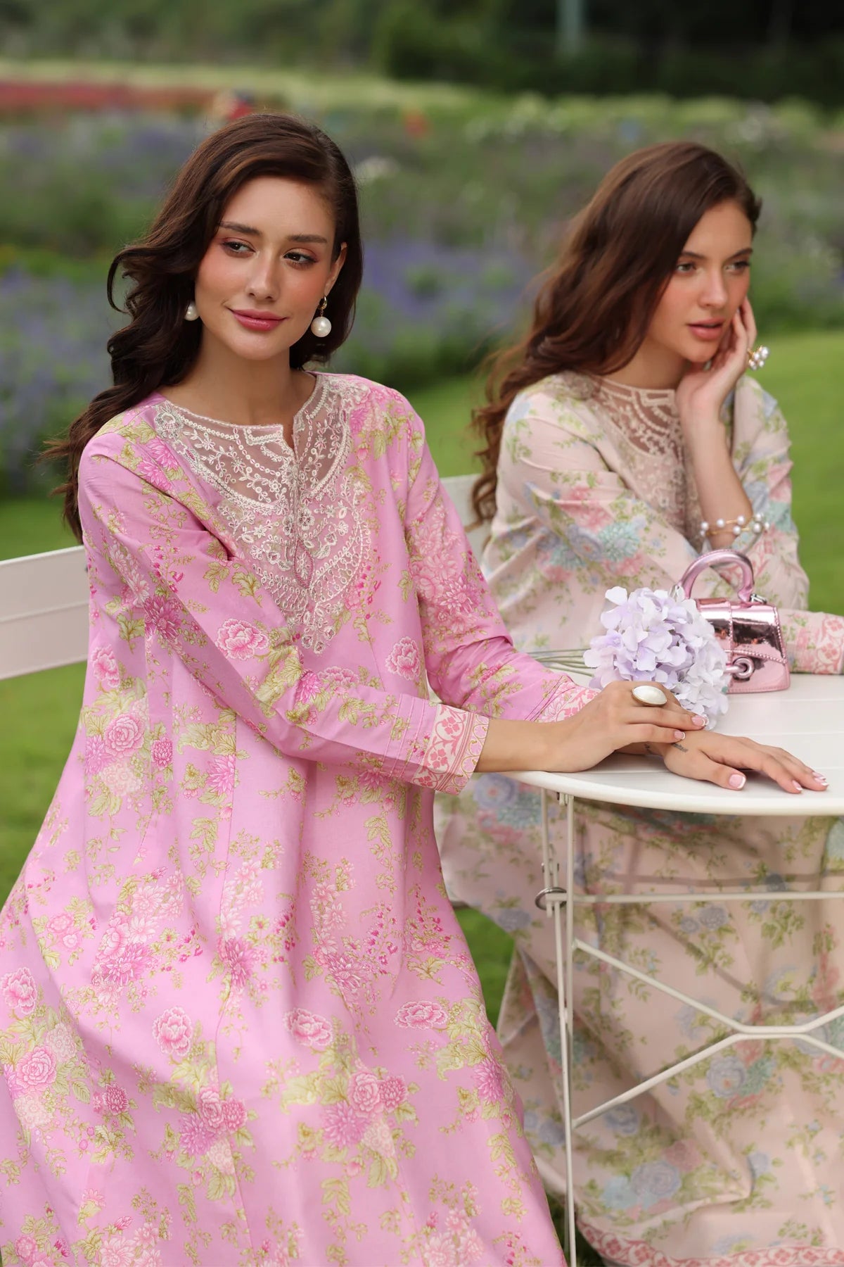 Two women seated three-quarter view Xenia pink floral lawn gown embroidered neckline festive wedding Pakistani suits Canada