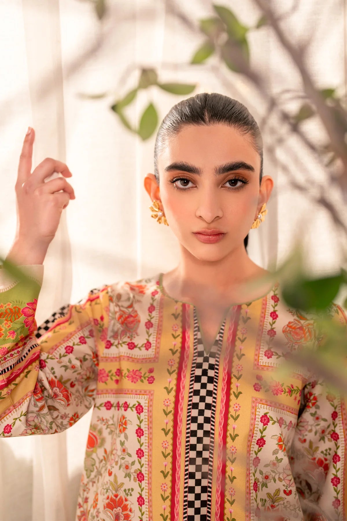 Woman portrait close-up model looking directly at camera, hand raised, neckline and upper chest print detail visible front Xenia Elia floral printed lawn Eid Indian suits online Canada