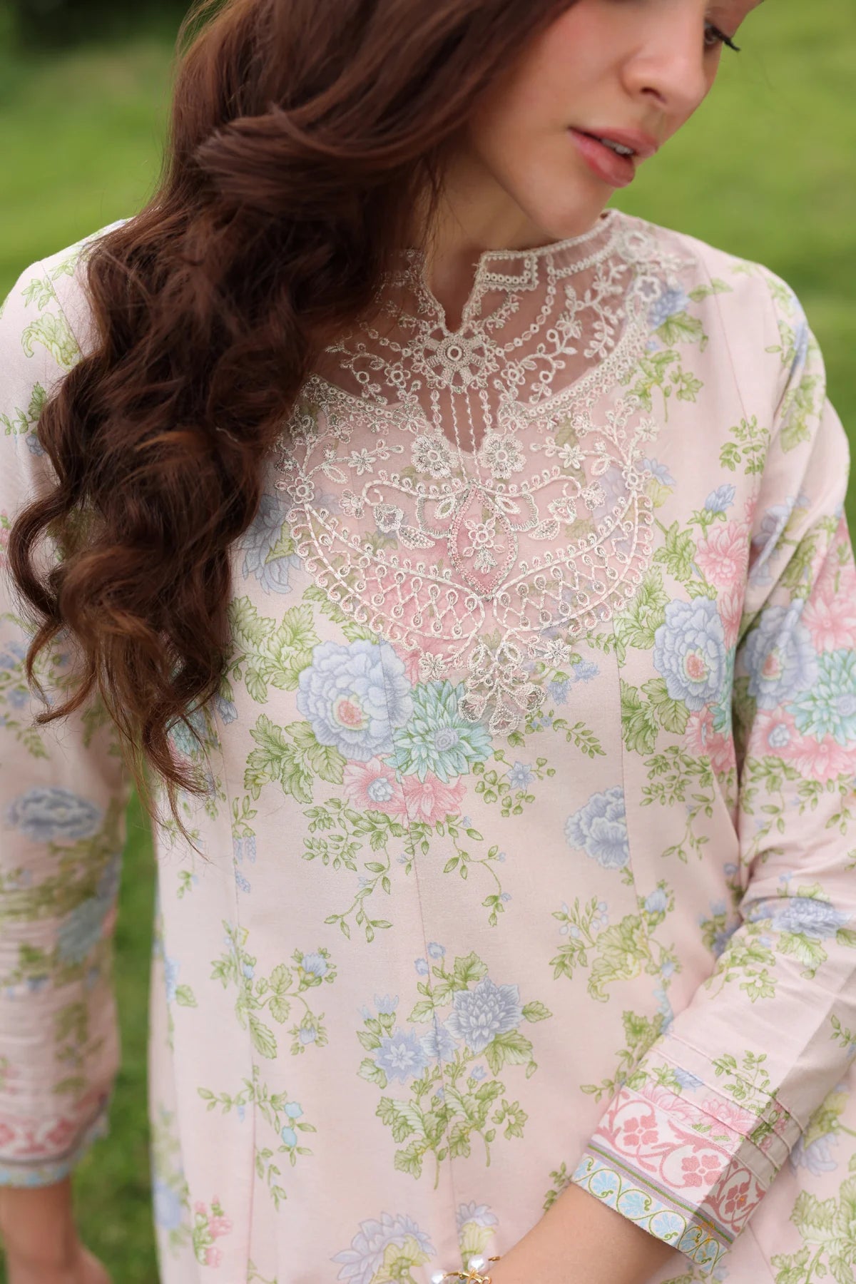 Close-up portrait of a model looking left with white crochet lace embroidered neckline  embroidered cuffs and  pastel floral print all clearly visible for Pakistan suits online Canada 