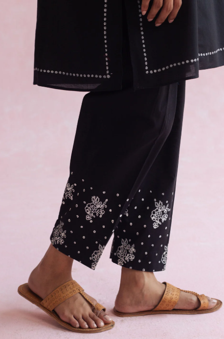 Black pants with white embroidery worn by a person on a light pink background